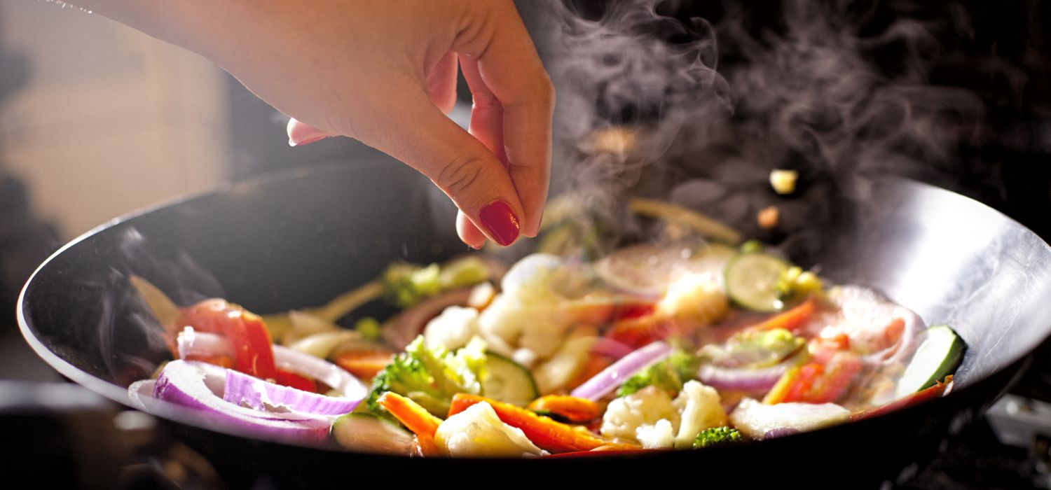 hand adding salt into a work with stir fry